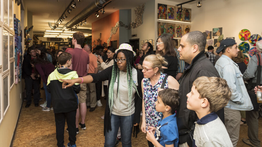 A group of small business owners press into the doorway of the new Amplify Latinx office suite. With broad smiles, they use large scissors to cut a blue ribbon marking the opening of the space. A plaque to the left announces the space, and the right side of the frame is full of colorful celebratory balloons.