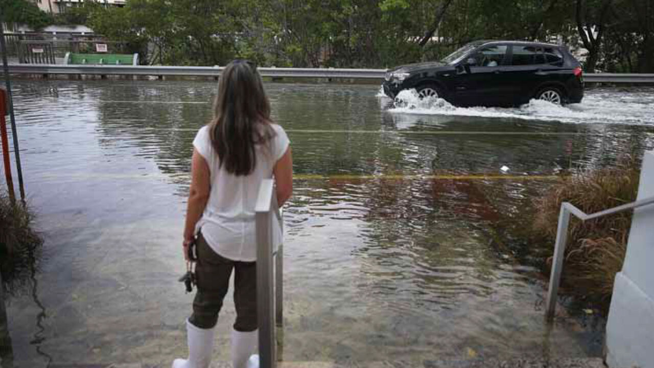 Woman standing on her front porch looking at a flooded street.