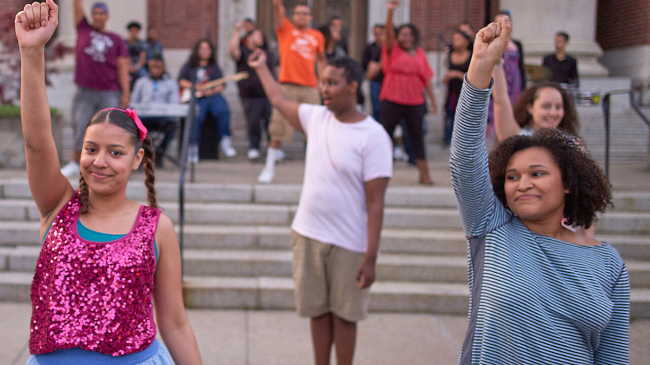 Kids pump their fists during a musical performance.