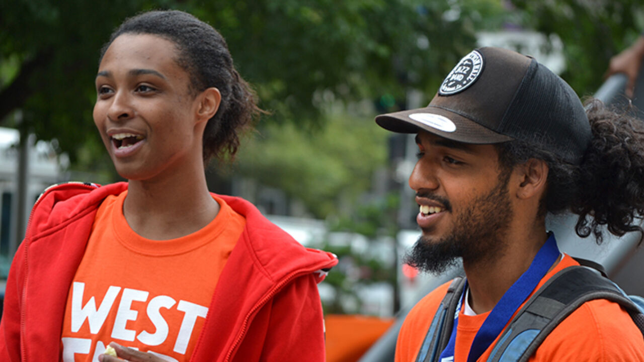 Two kids smile and talk outside.