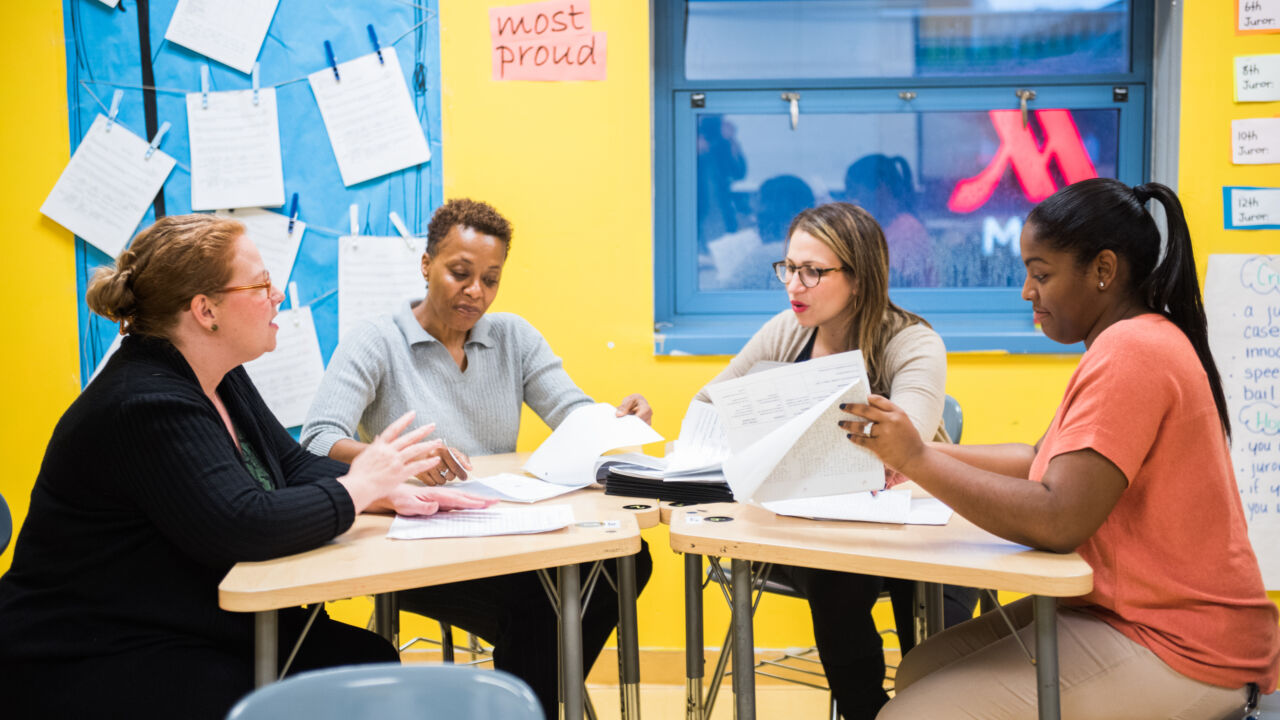 Four teachers work around a table looking at papers.