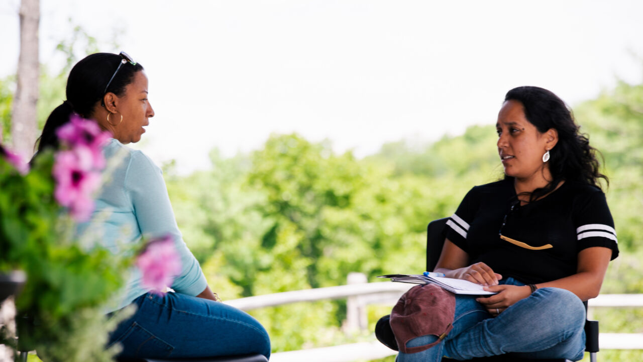 Two women talk to each other on a porch.