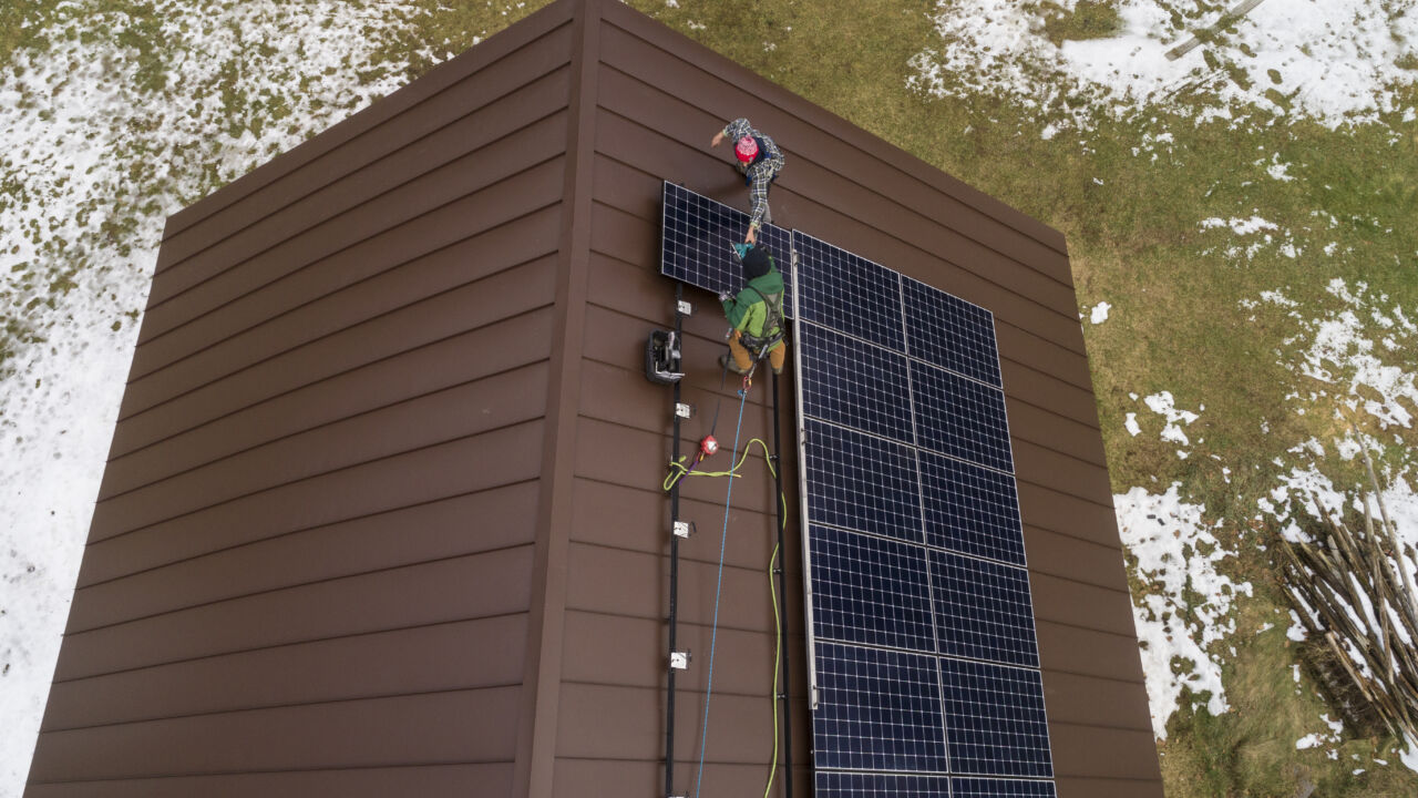 Two men install solar panels on the roof of a home.