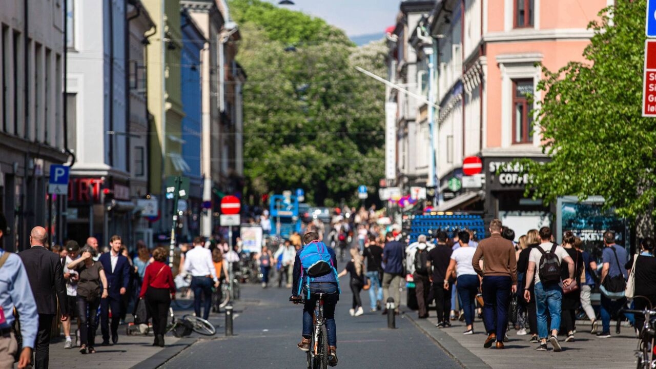 Biker goes down a street with no cars on it, only people, in Oslo.