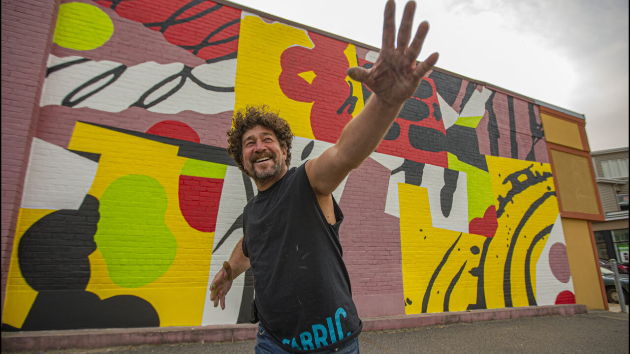 A man poses happily with a mural.