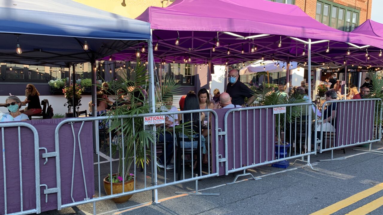 People dining outside a restaurant on a section of a street that is blocked off with a fence.