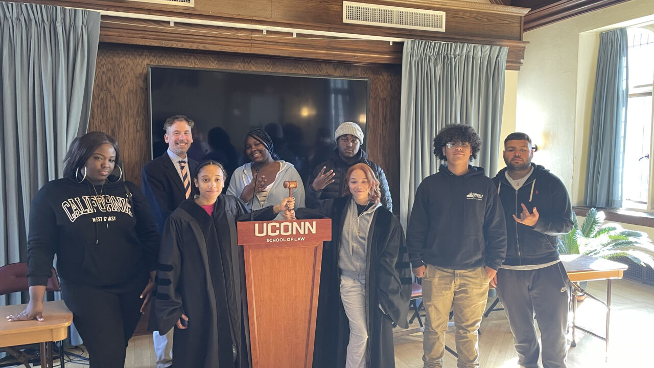 Students participating in Moot Court exercise at the University of Connecticut School of Law. They are posing for the camera next to a UCONN school of law podium.
