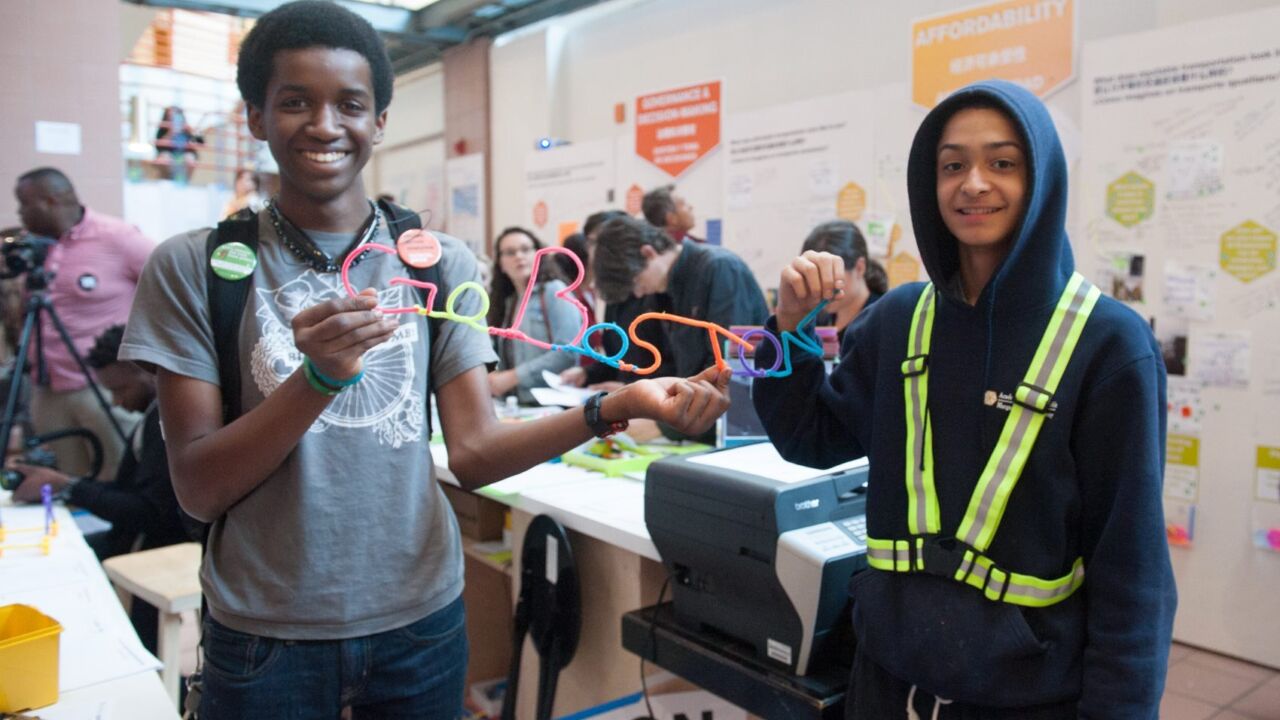 Two teenagers hold up a straw sign that reads "Go Boston 2030".