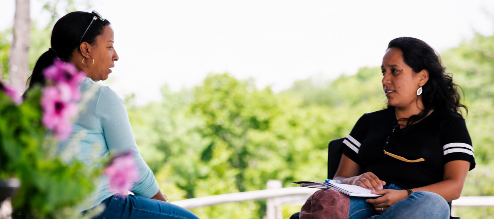Two women talk to each other on a porch.