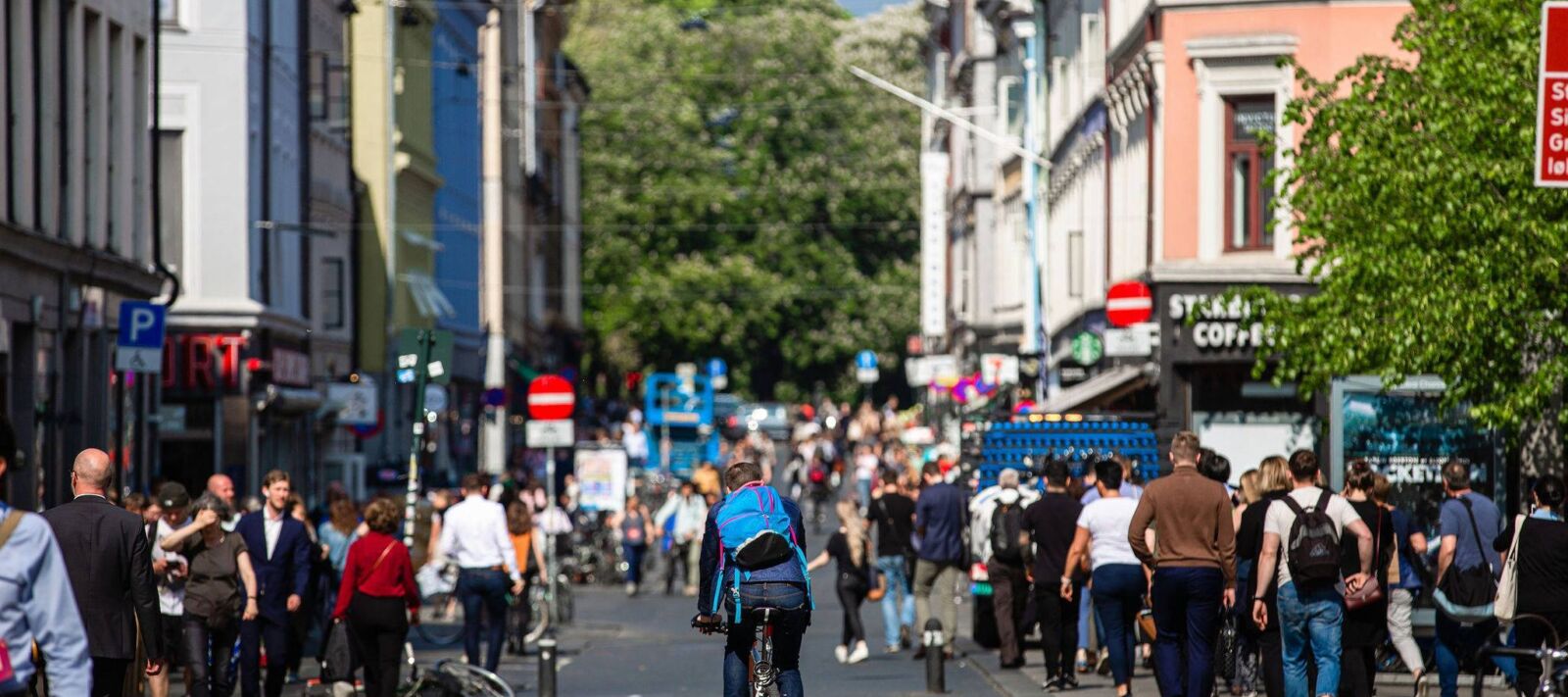 Biker goes down a street with no cars on it, only people, in Oslo.