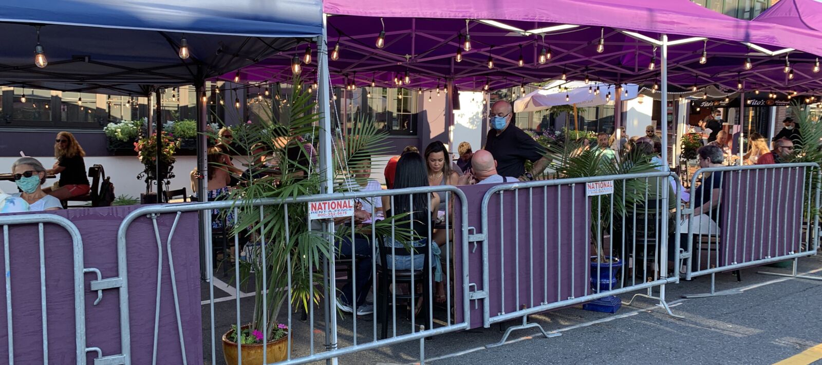 People dining outside a restaurant on a section of a street that is blocked off with a fence.