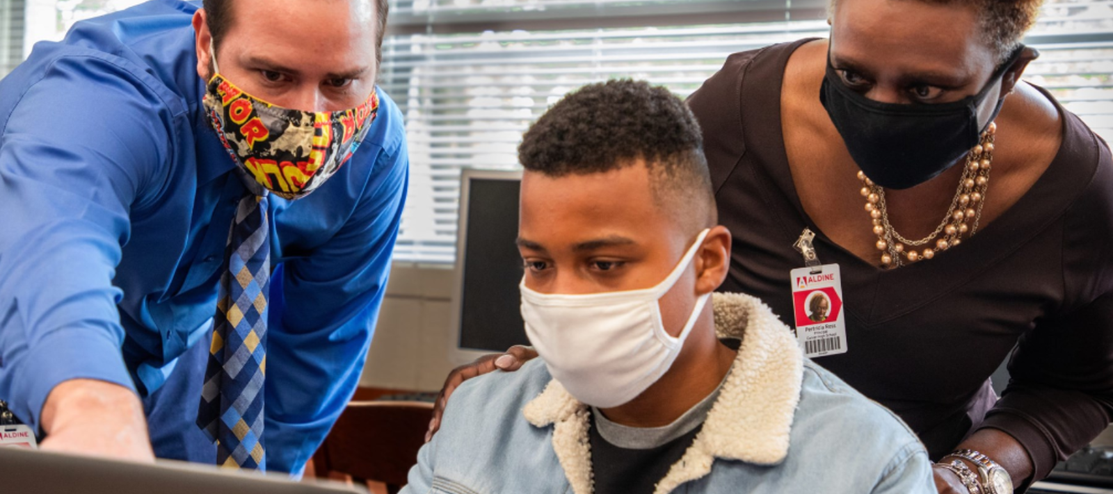 a masked student works with masked teachers.