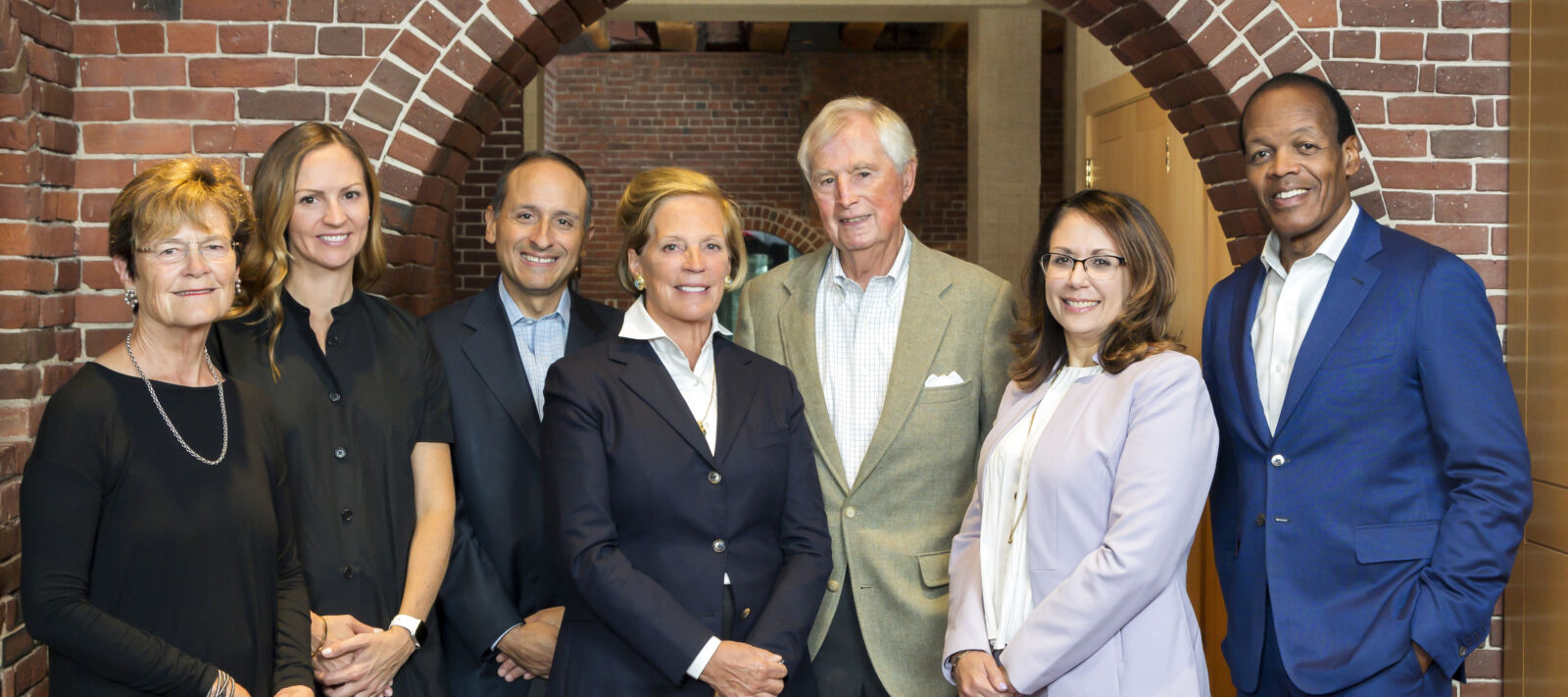 Four women and three men posed beneath a brick archway.