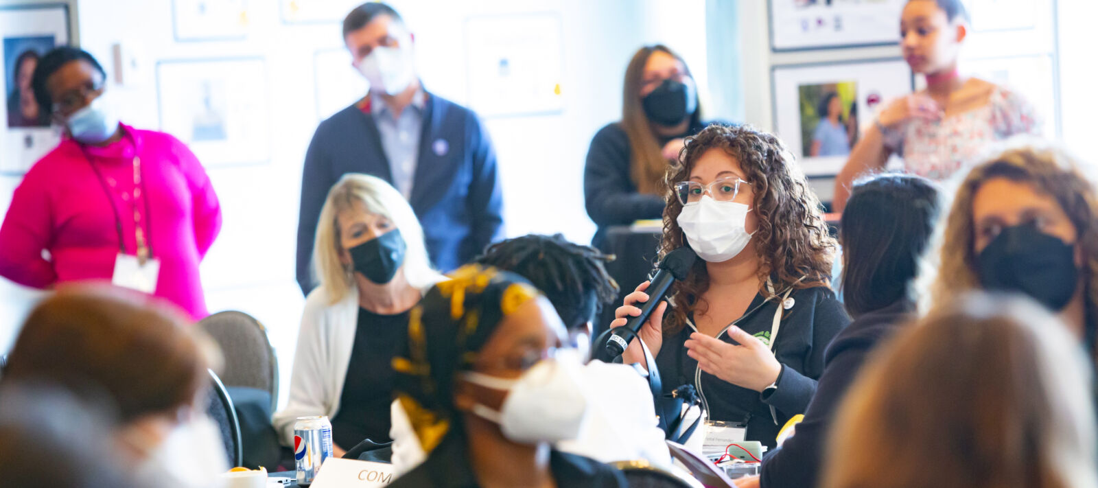 A masked speaker speaking to a room full of people at a spring convening.