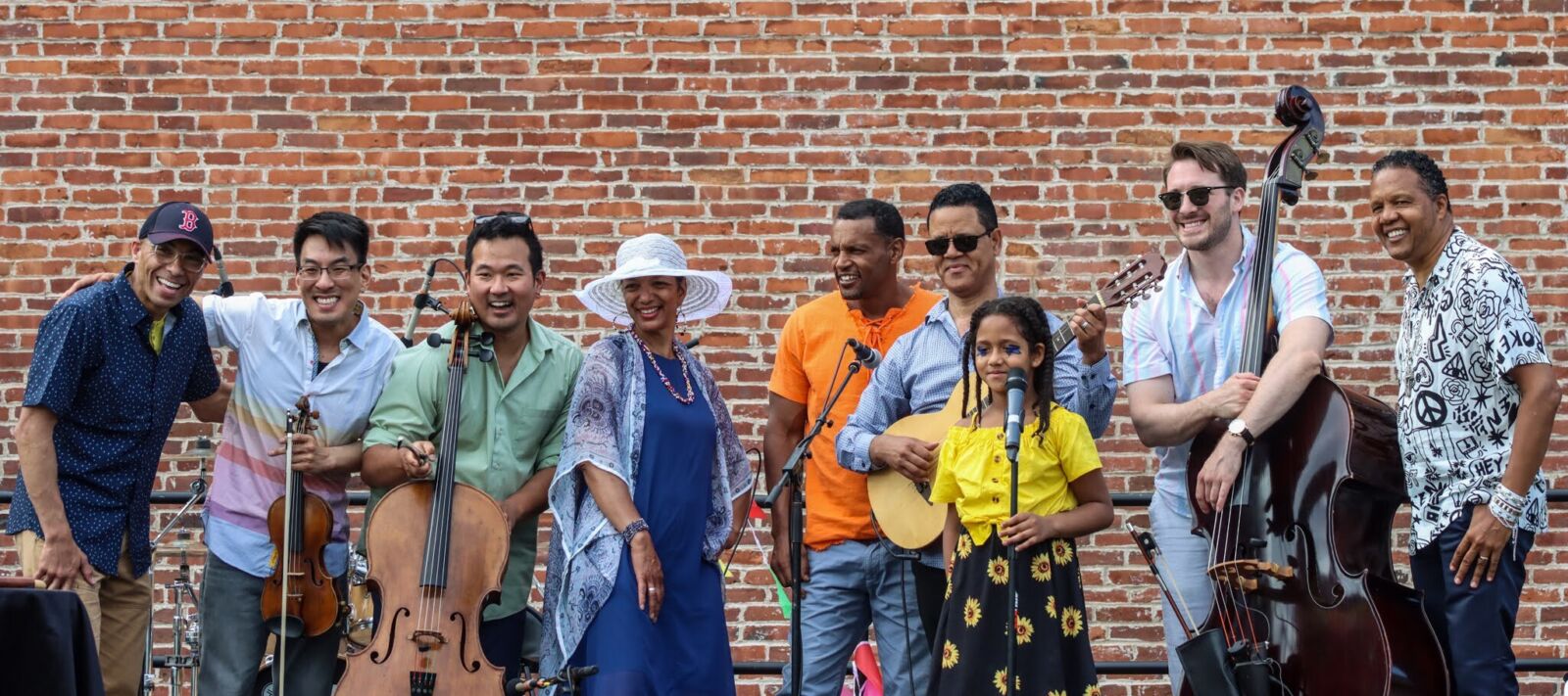 Several musicians standing on a stage outdoors holding instruments