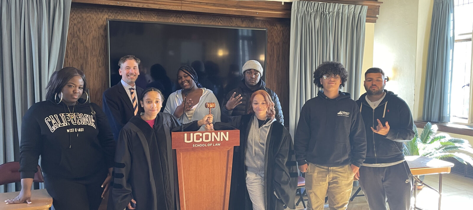 Students participating in Moot Court exercise at the University of Connecticut School of Law. They are posing for the camera next to a UCONN school of law podium.