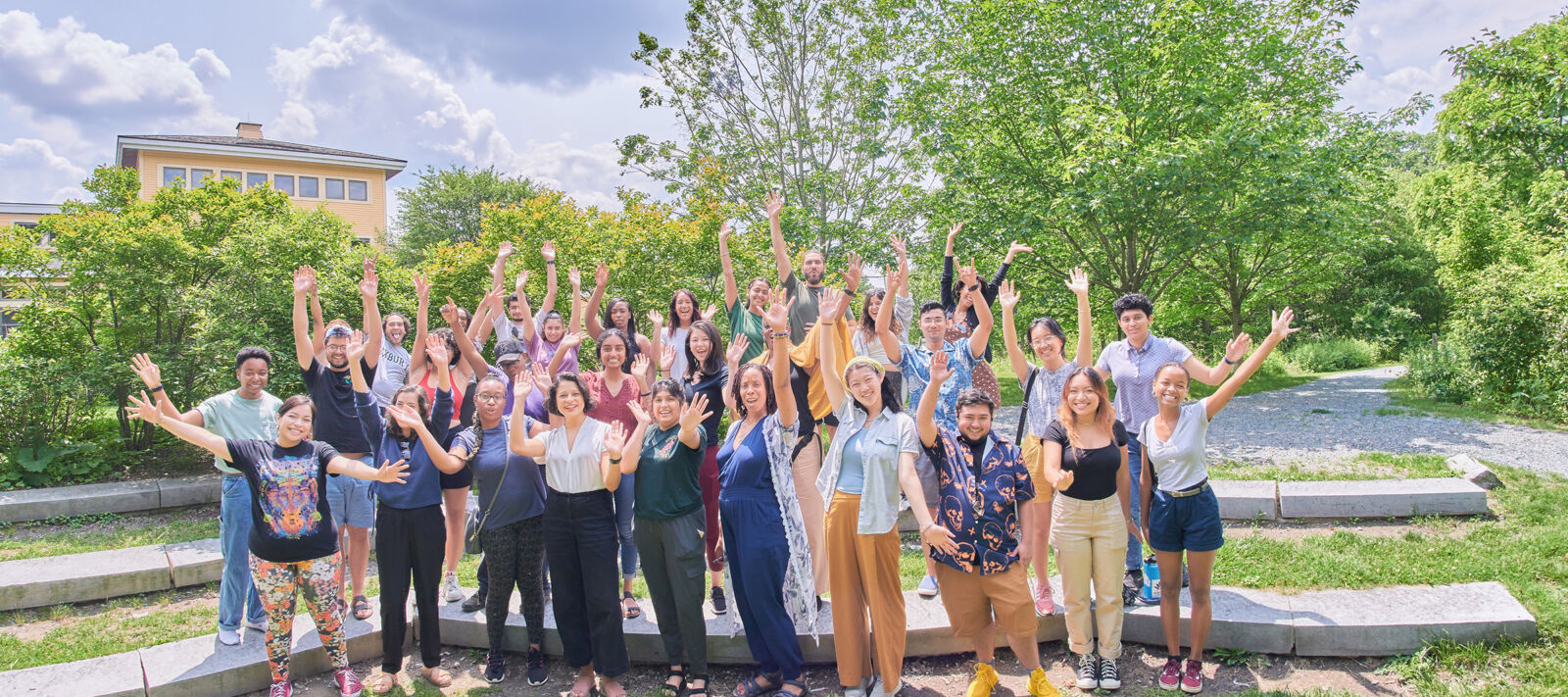 A group of people of color standing outside on green grass, acting excited with their arms in the air.