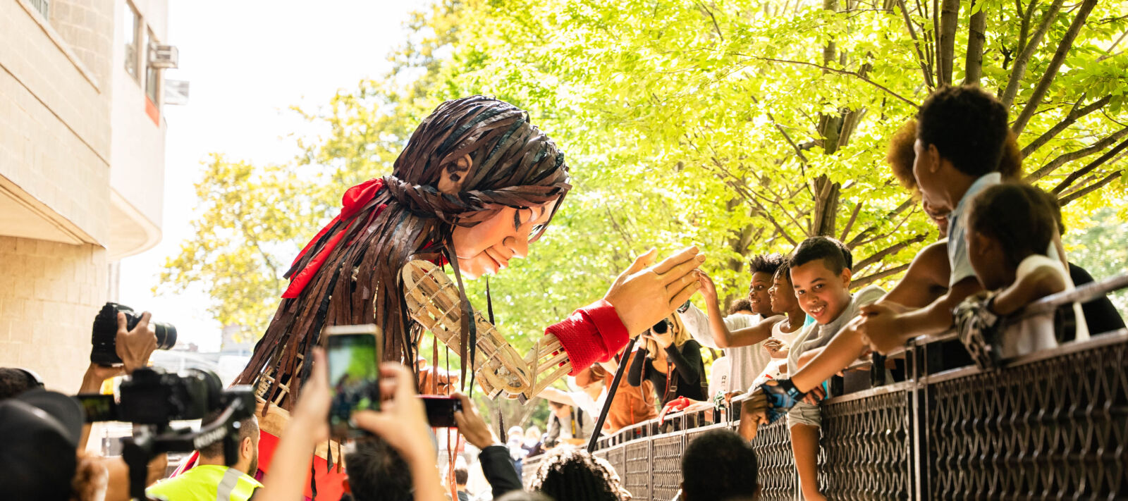 A large puppet of a 10-year-old Syrian girl named Little Amal interacts with a crowd.