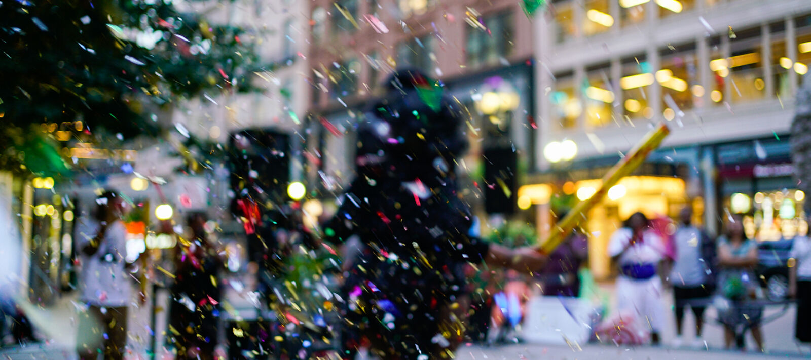 A blurry scene of performers in a public urban space with colorful confetti.