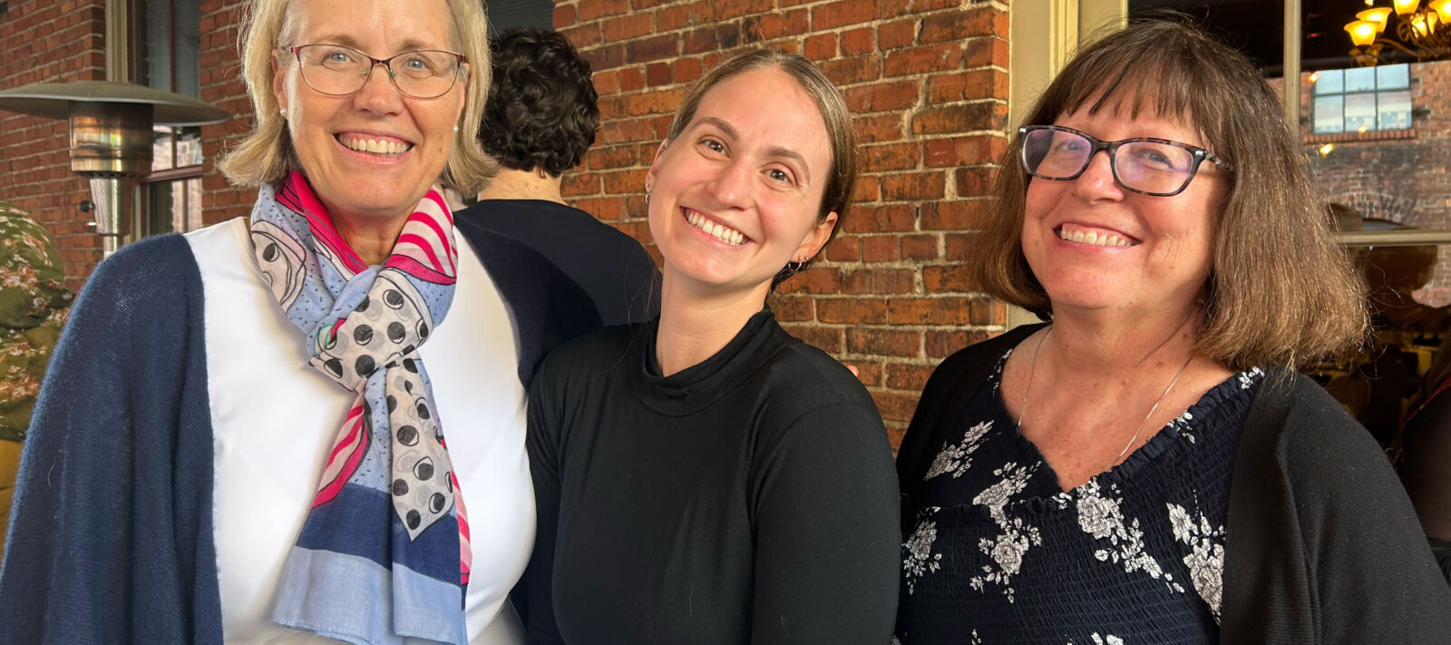 Three white women of varying ages smiling and posing for a photo on an outdoor balcony.
