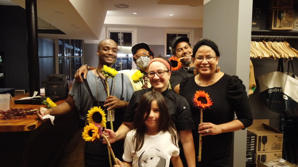 A small group of chefs and artists pose in a restaurant holding sunflowers