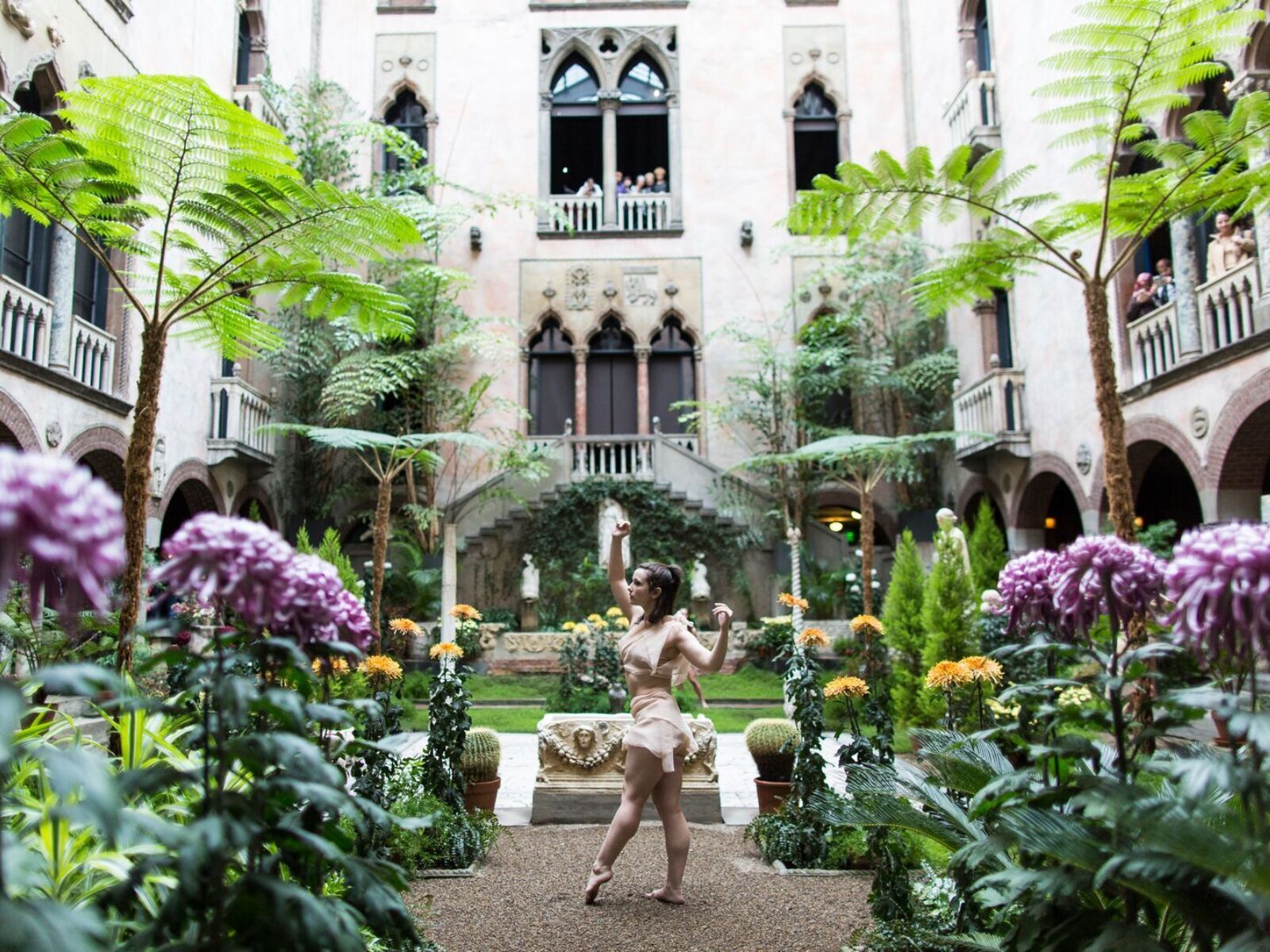 A beautiful indoor courtyard garden within Boston's Isabella Stewart Gardner Museum. A solo ballerina dancer moves among purple and yellow flowers.