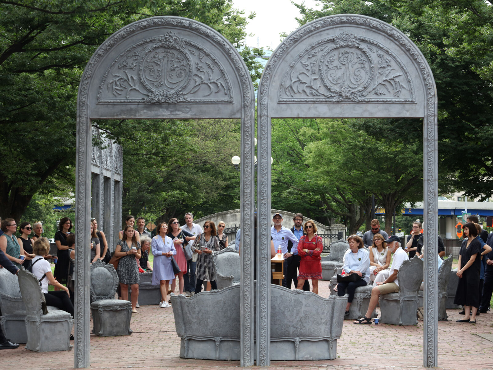 A group of people are standing in a park are looking at a public art exhibit by American visual artist, Liz Glynn.