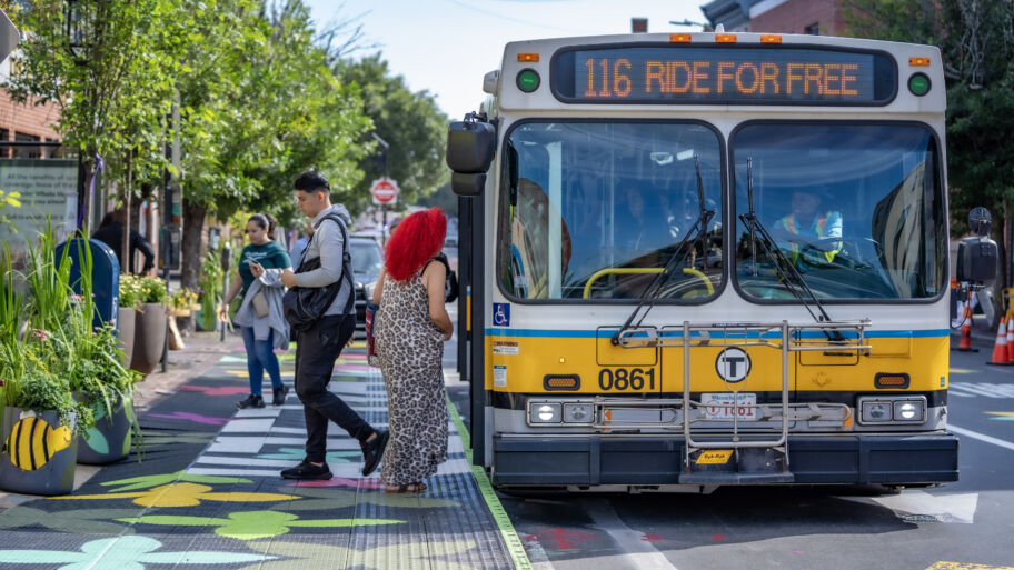 Someone getting on and off a city bus at a bus stop that has a painted elevated platform and bus shelter with colorful flowers